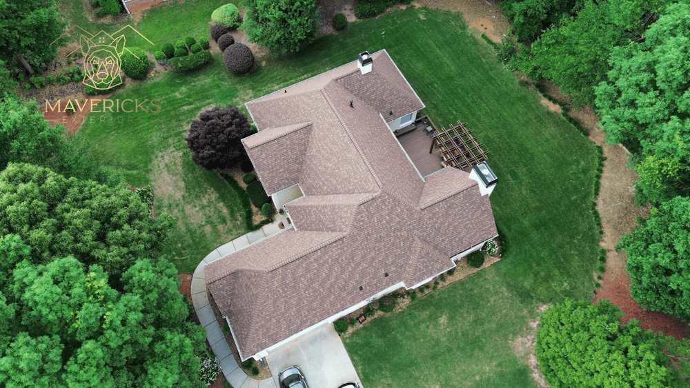 Aerial view of a home with a new brown shingle roof surrounded by trees